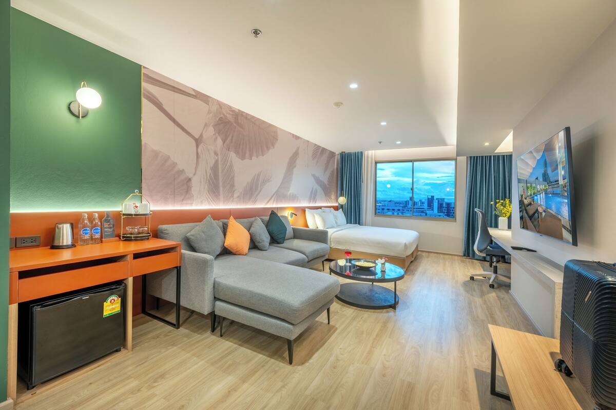 Une chambre d’hôtel moderne équipée d’un canapé, d’un bureau, d’un petit réfrigérateur, d’un coin café, d’une télévision et offrant une vue sur la ville.