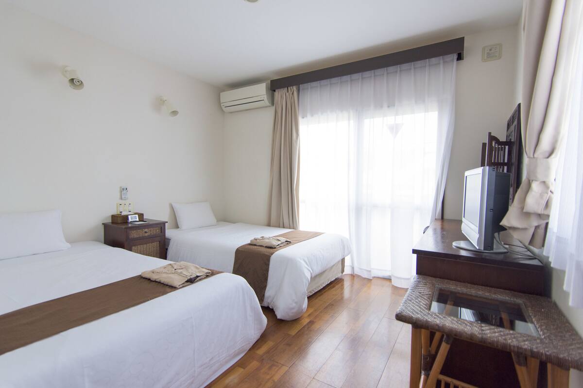 Een hotelkamer met twee bedden, een bureau met een televisie en een airconditioning aan de muur.