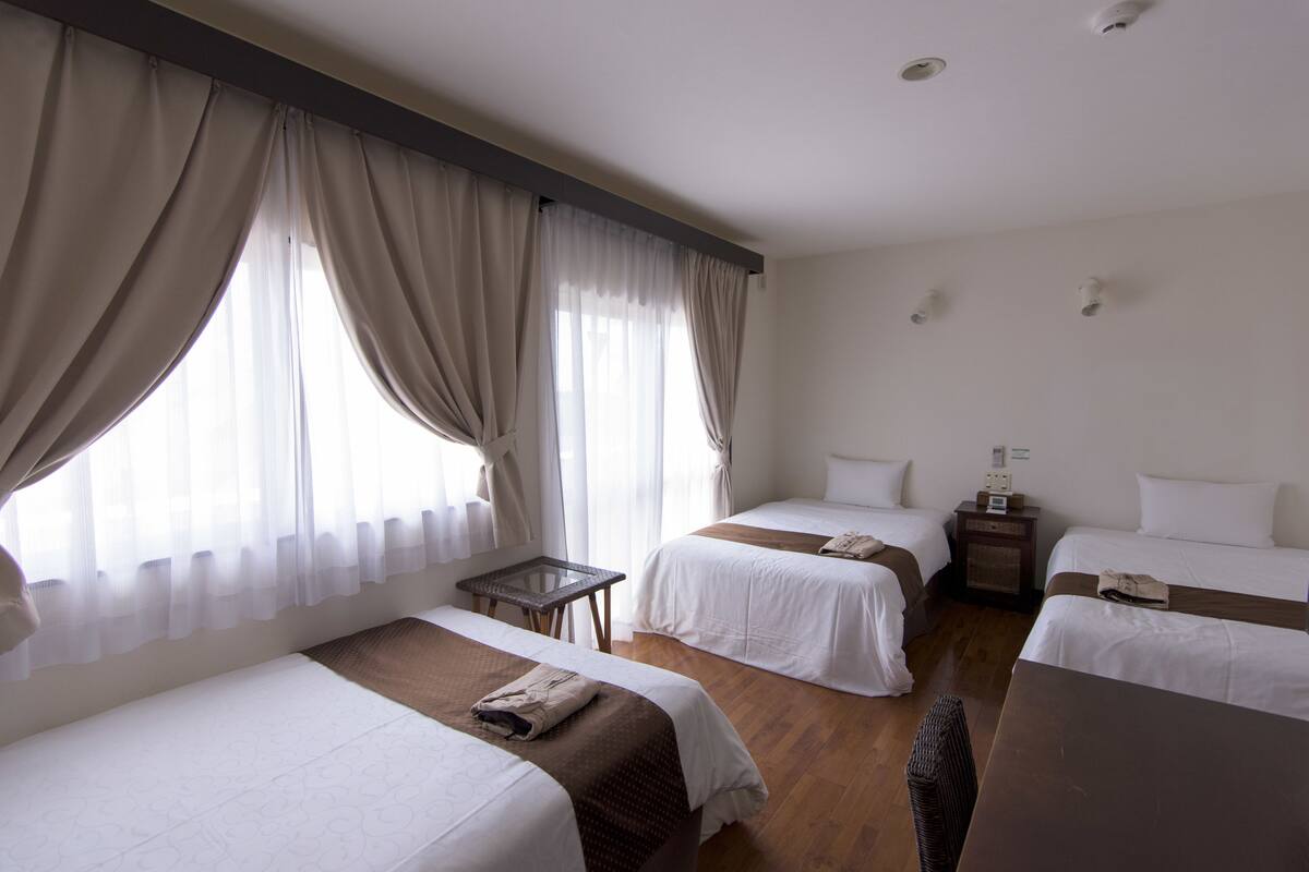 Een hotelkamer met twee enkele bedden, een tafeltje, een nachtkastje en een raam met gordijnen.