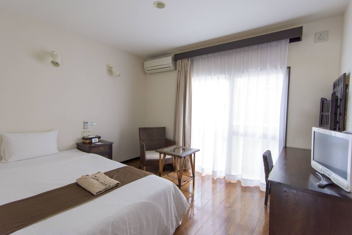Hotelkamer met een bed, een stoel, een bureau met een computer en een raam met gordijnen.