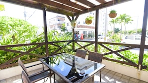 Eine Terrasse im Freien mit Korbmöbeln, einem Glastisch und hängenden Pflanzen.