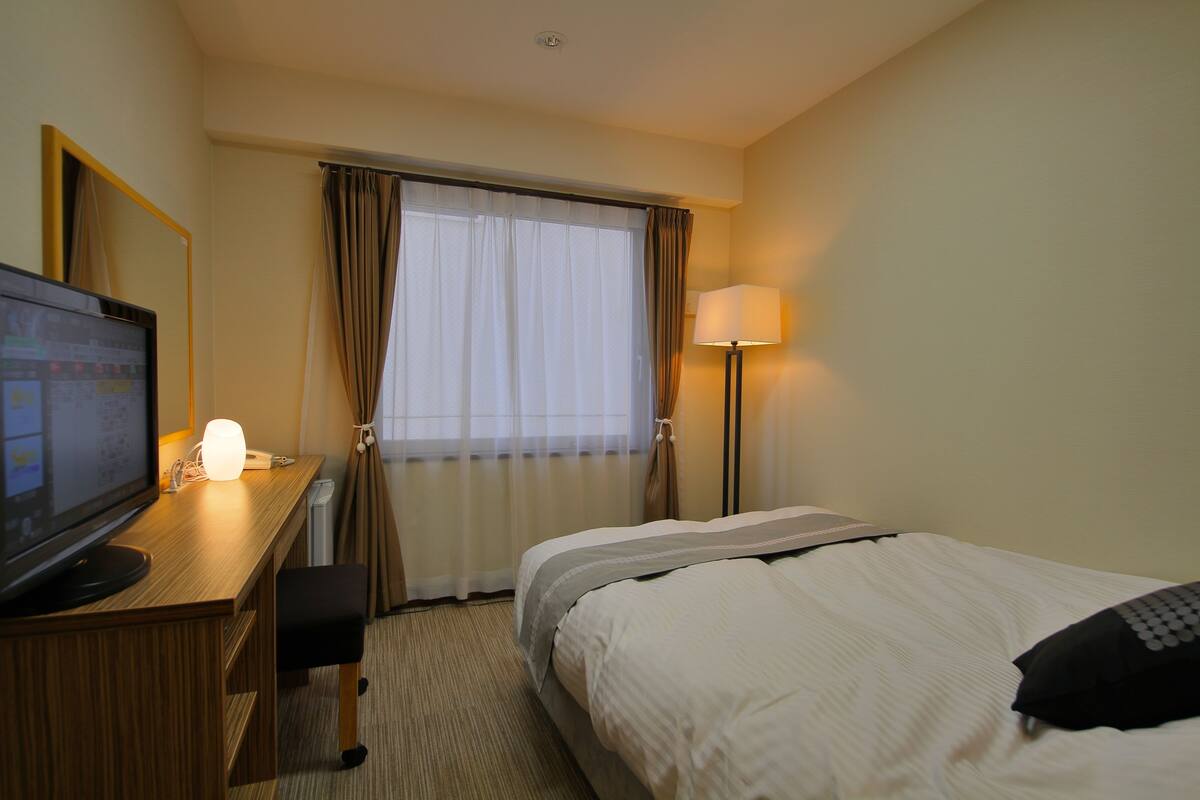A hotel room with a bed, a desk with a computer, a TV, and a lamp.
