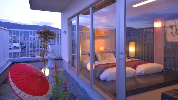 Un balcón con una sombrilla roja, una cama con almohadas y vistas a montañas.