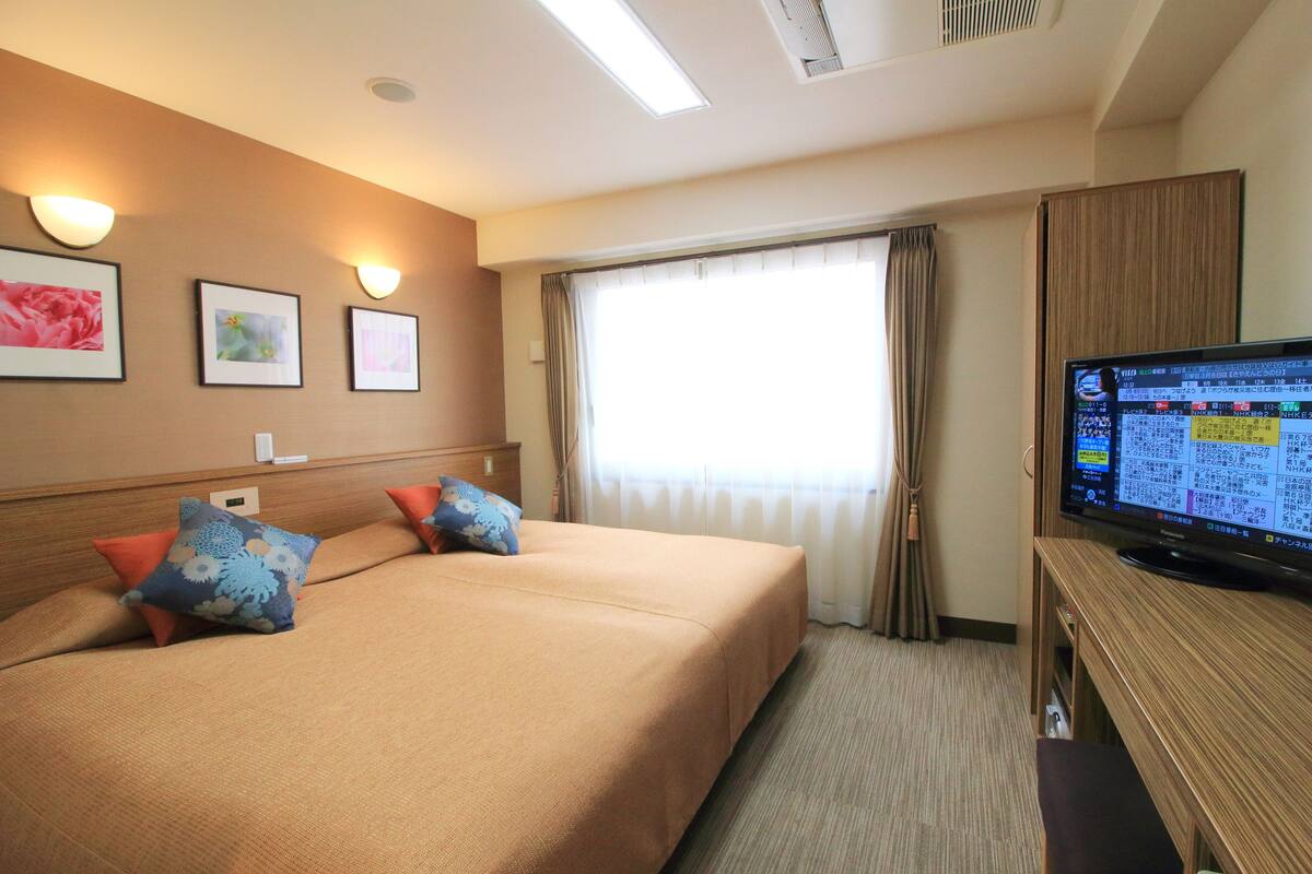 A hotel room with a bed, pillows, a television, and a window with curtains.