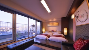 Una habitación de hotel moderna con un ventanal grande, un sofá, una cama con sábanas blancas y una almohada roja.