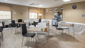 Un comedor con mesas y sillas, un reloj en la pared y una máquina de café.