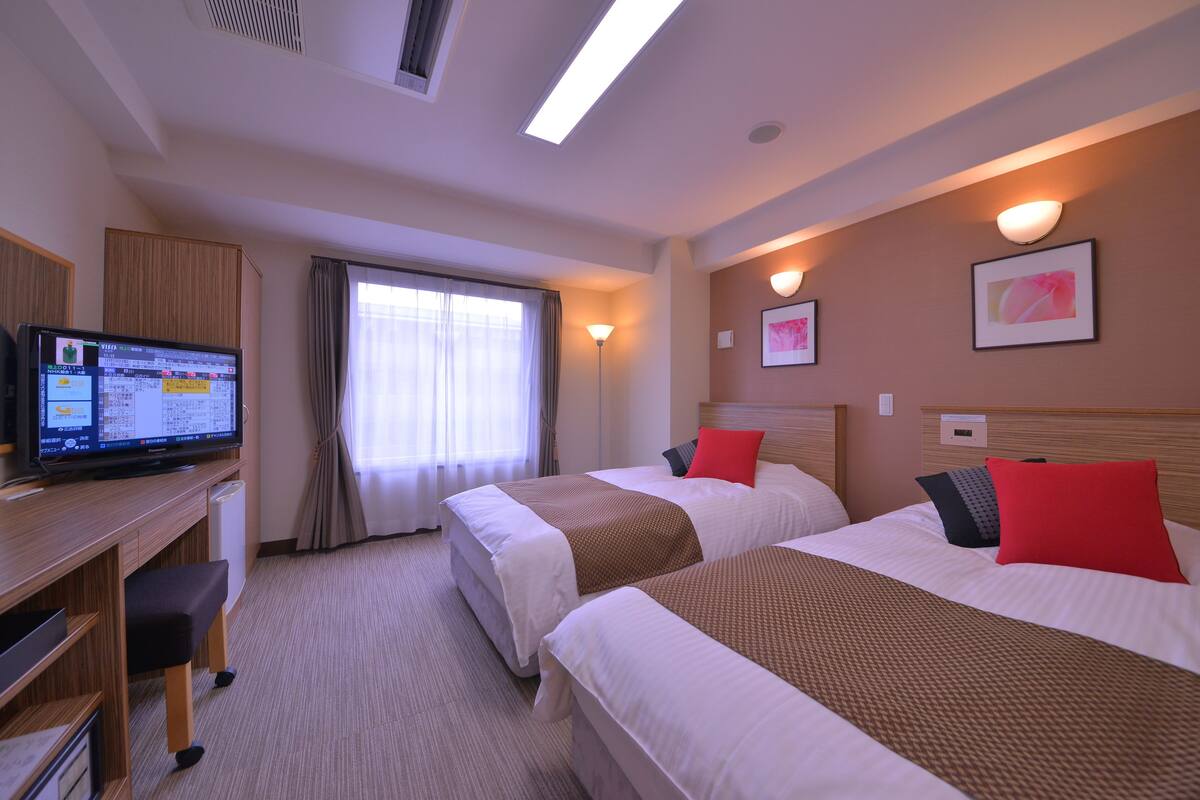 A hotel room with two beds, a desk with a computer, and a window with curtains.