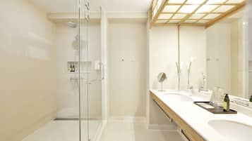 Un baño moderno con cabina de ducha de vidrio, un espejo grande y un tocador con lavamanos y encimera.