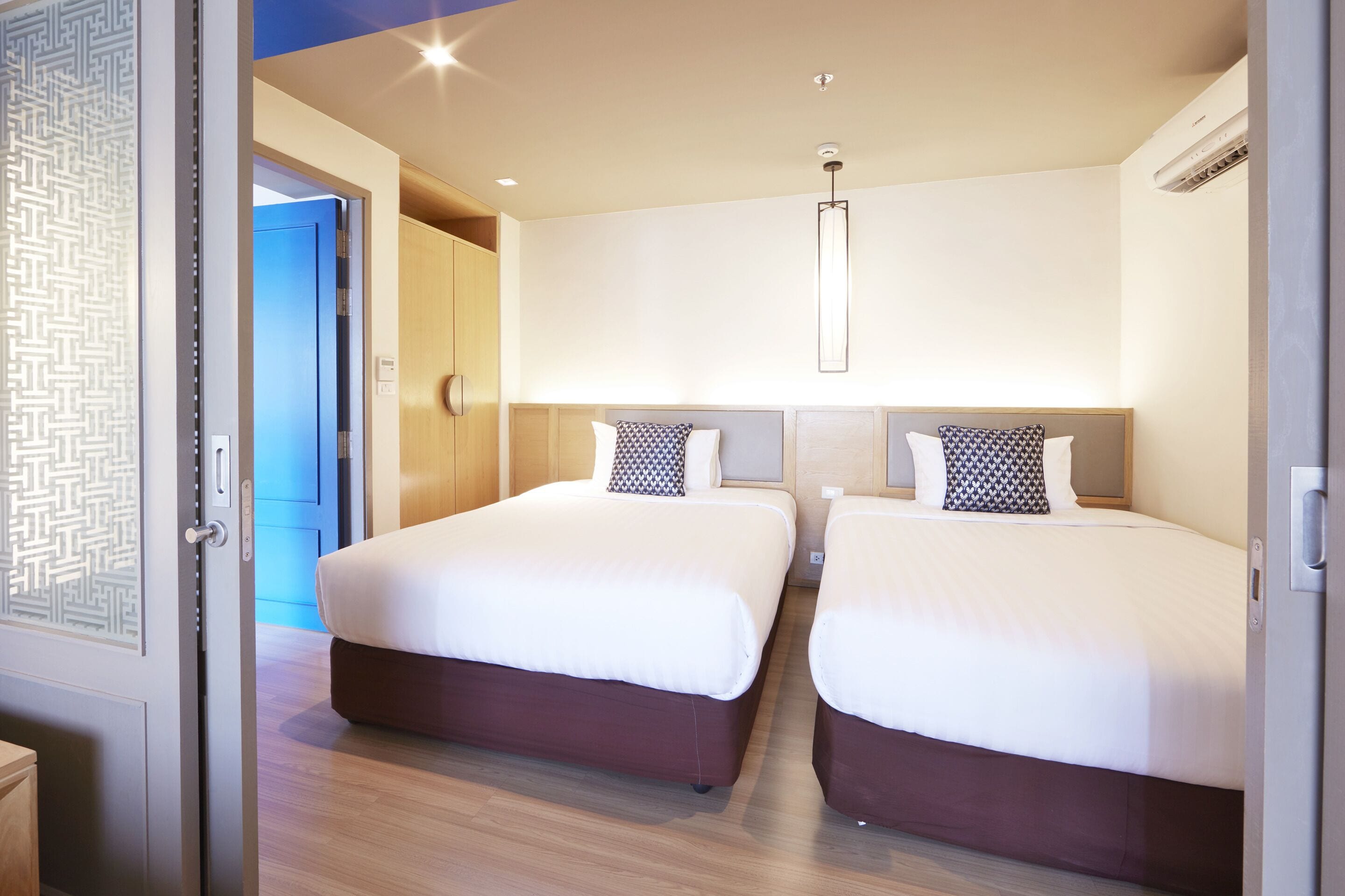 A hotel room with two beds, a modern light fixture, and a door with a geometric pattern.