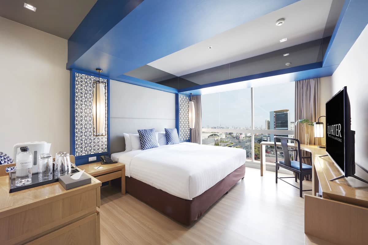 A modern hotel room with a large bed, a desk with a computer, and a city view.
