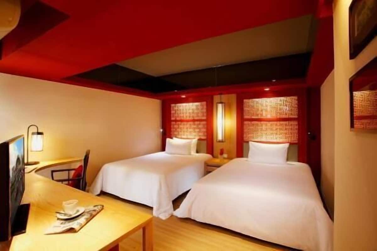 A hotel room with two beds, a desk, and a television.