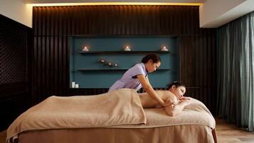 A massage therapy room with a massage table, a person providing a massage, and a shelf with candles in the background.