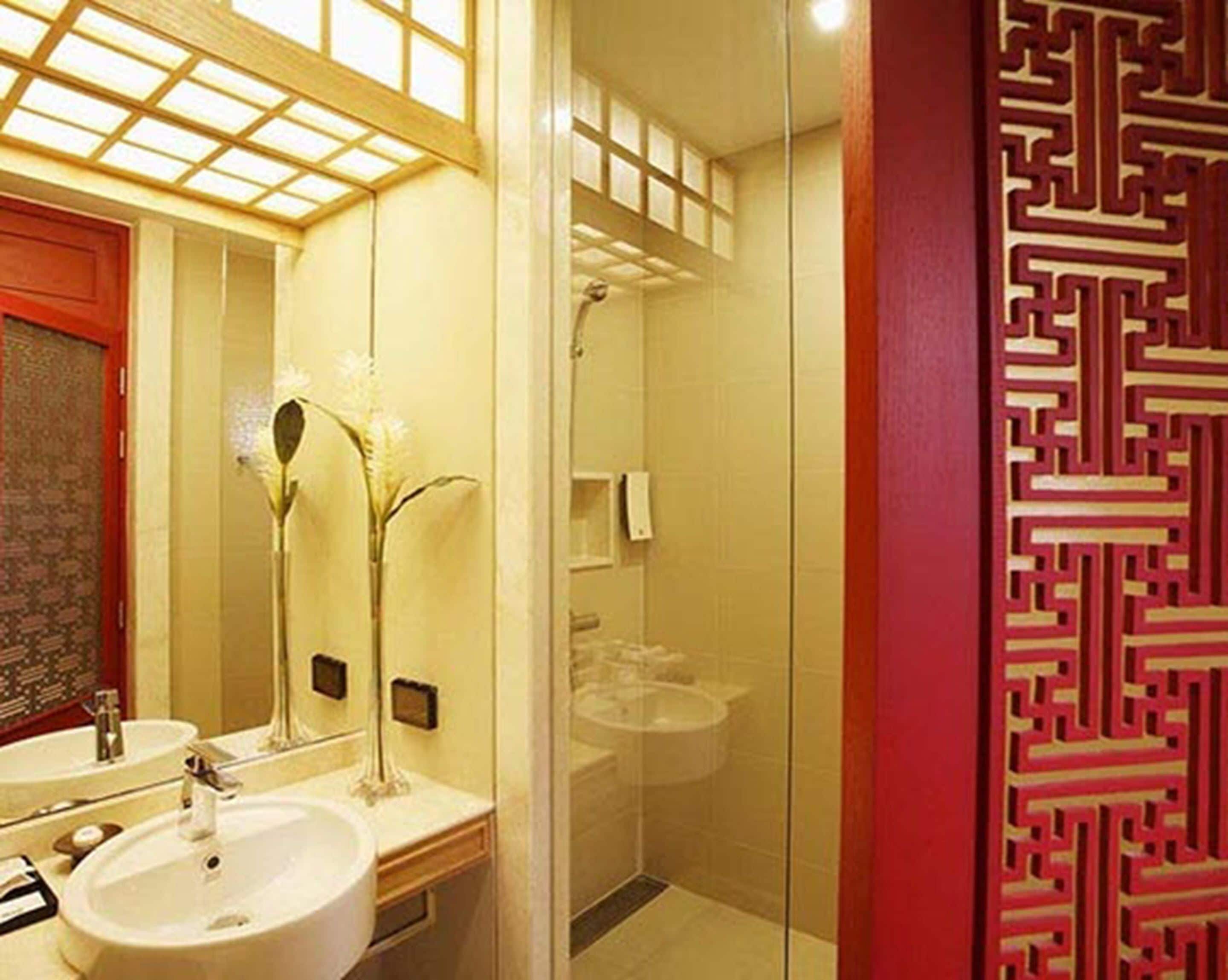 Ein Badezimmer mit Spiegel, zwei Waschbecken, einer Dusche und einer dekorativen Wandverkleidung.