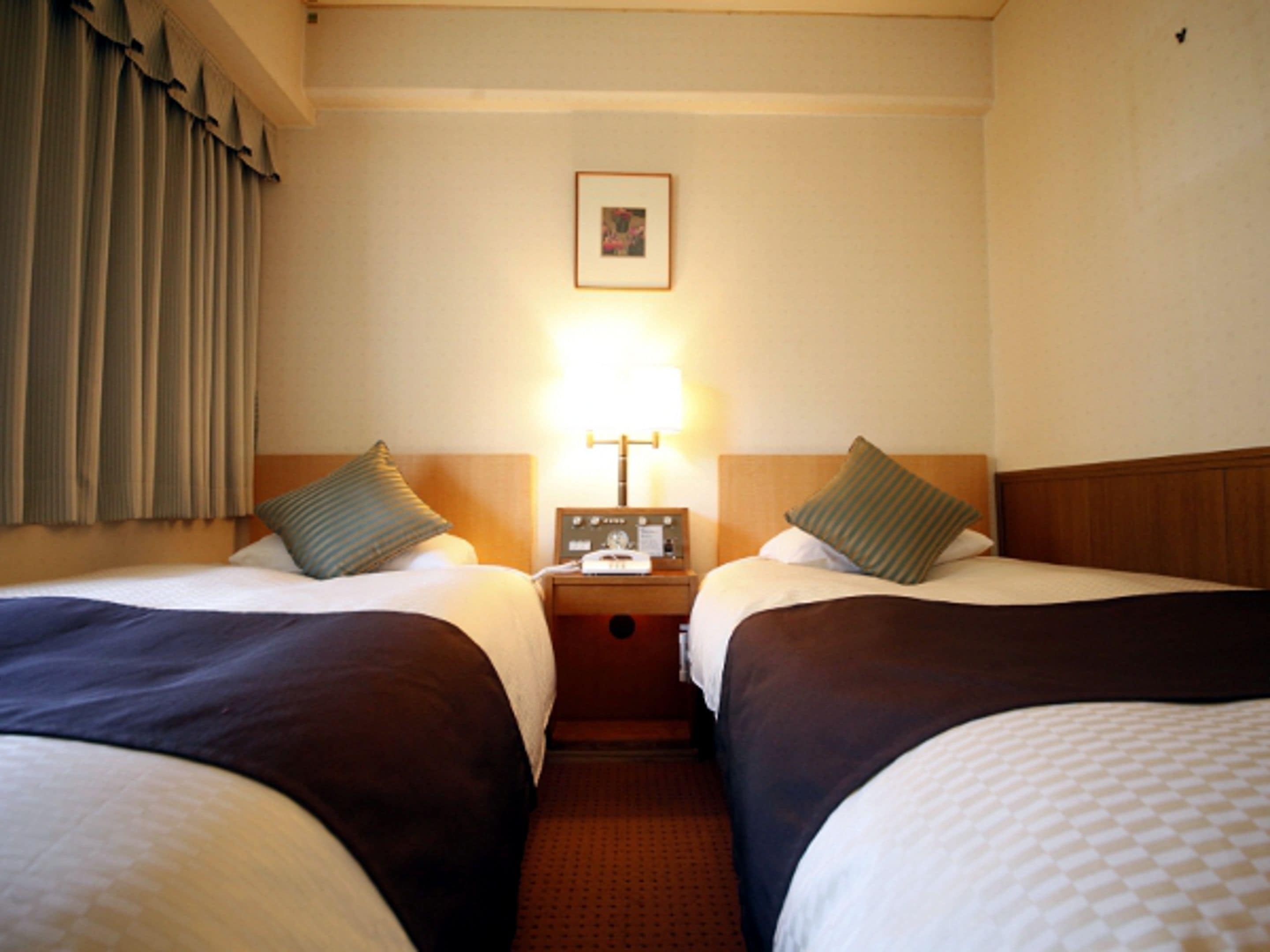 A hotel room with two beds, each with a pillow and a bedside table with a lamp.