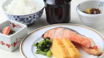 A plate with salmon, green vegetables, and a yellow side dish, alongside bowls of rice and another dish with meat and vegetables.