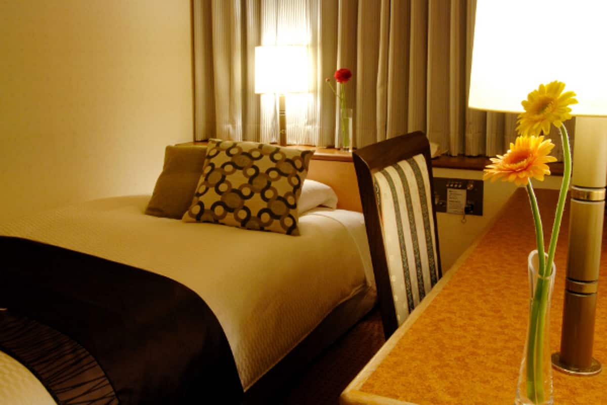 A hotel room with a bed, a chair, a table, and a vase with flowers.