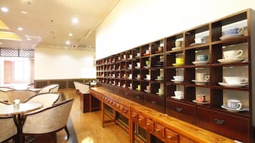 Un hall de hotel con un largo mostrador de recepción de madera, varias áreas de descanso y una pared de estanterías que exhiben tazas y platillos.