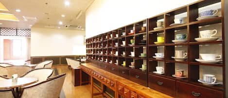 A hotel lobby with a long wooden reception desk, multiple seating areas, and a wall of shelves displaying various cups and saucers.