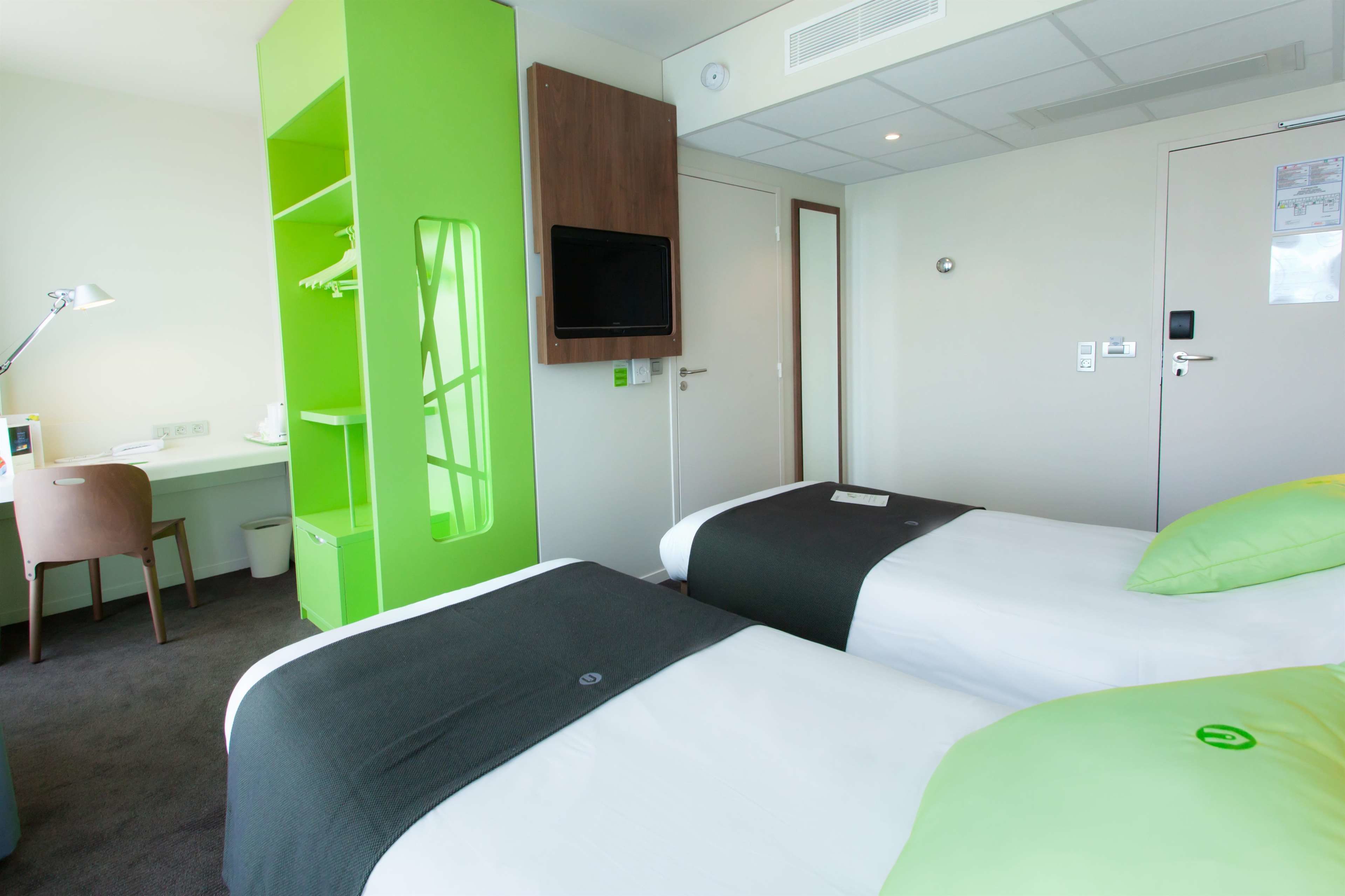 A hotel room with two beds, a desk, a chair, and a TV mounted on the wall.