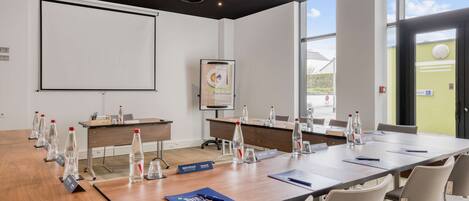 A conference room with a long table, chairs, water bottles, name tags, and a projector screen.