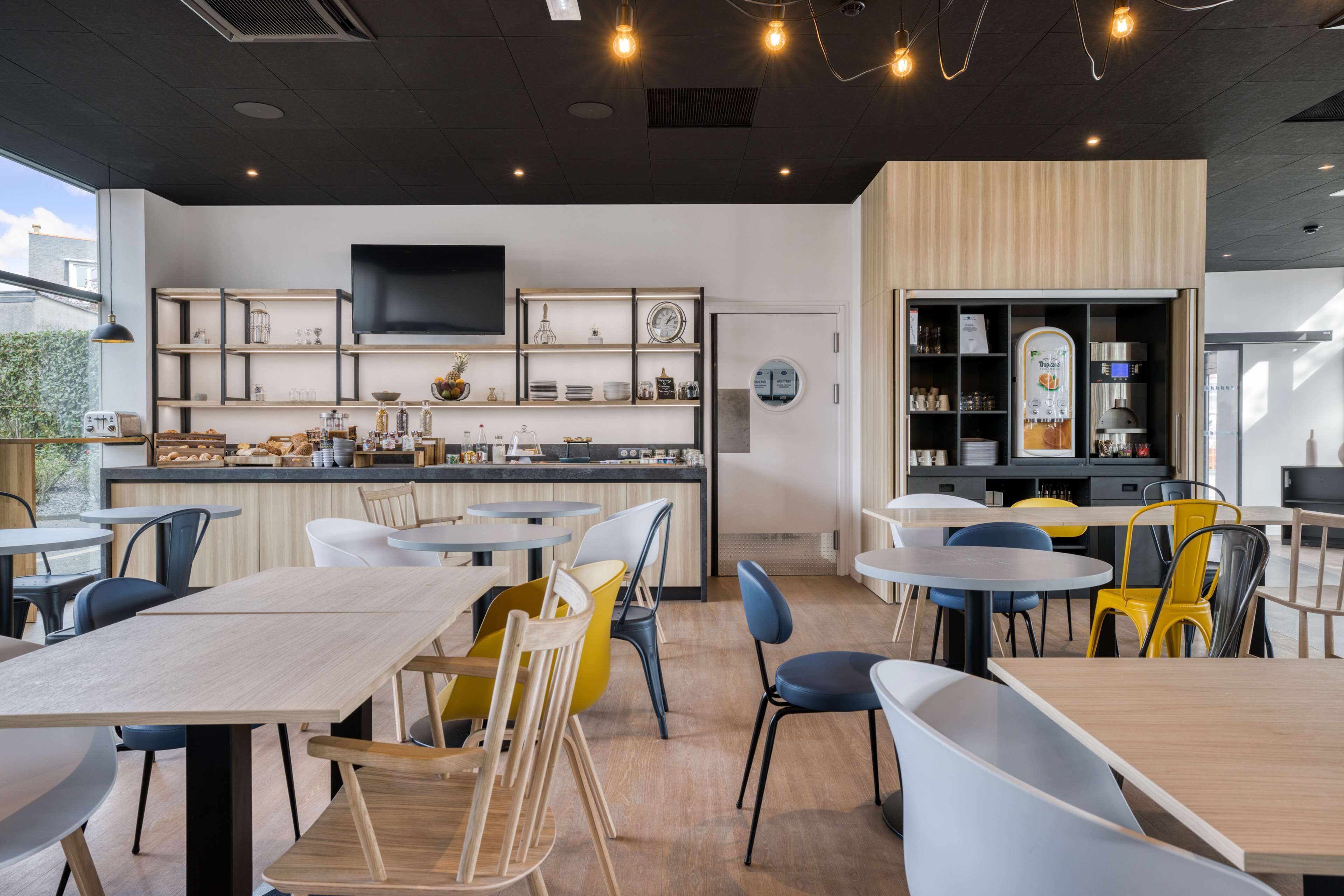 Un café moderne doté d’un bar, de différents espaces pour s’asseoir et d’un écran de télévision.