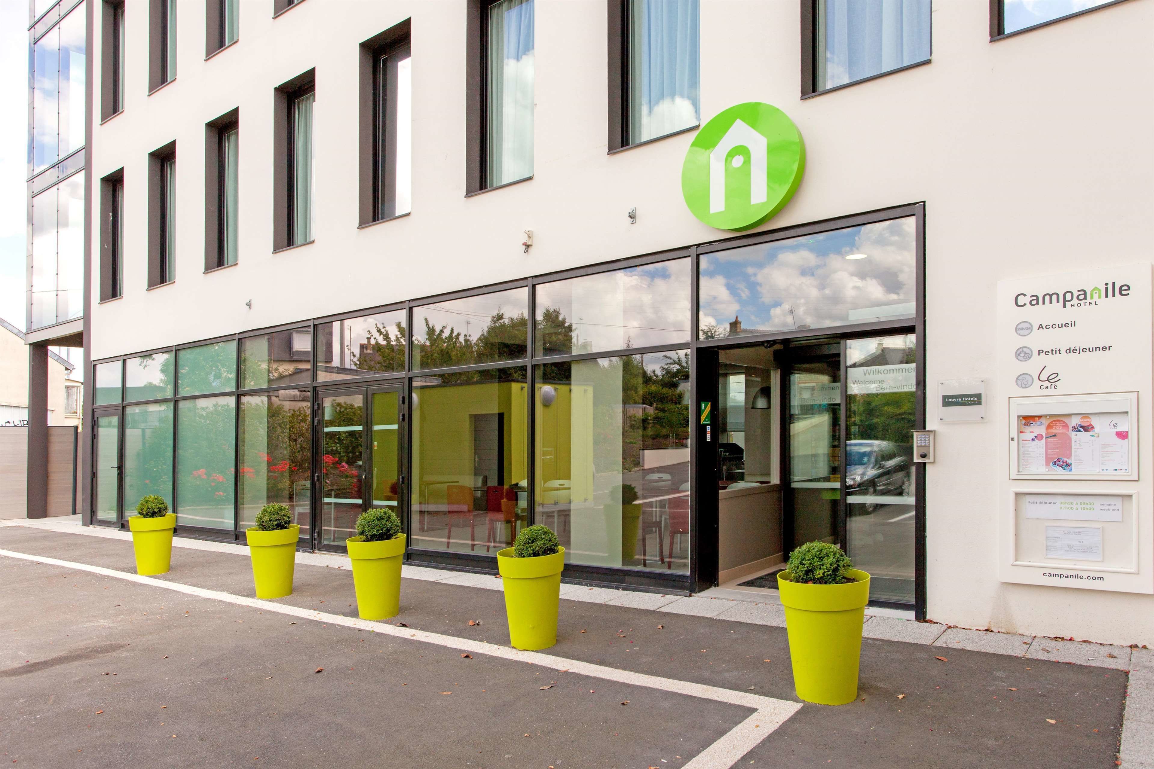 A modern hotel with a glass facade, a green logo, and a signboard listing amenities.