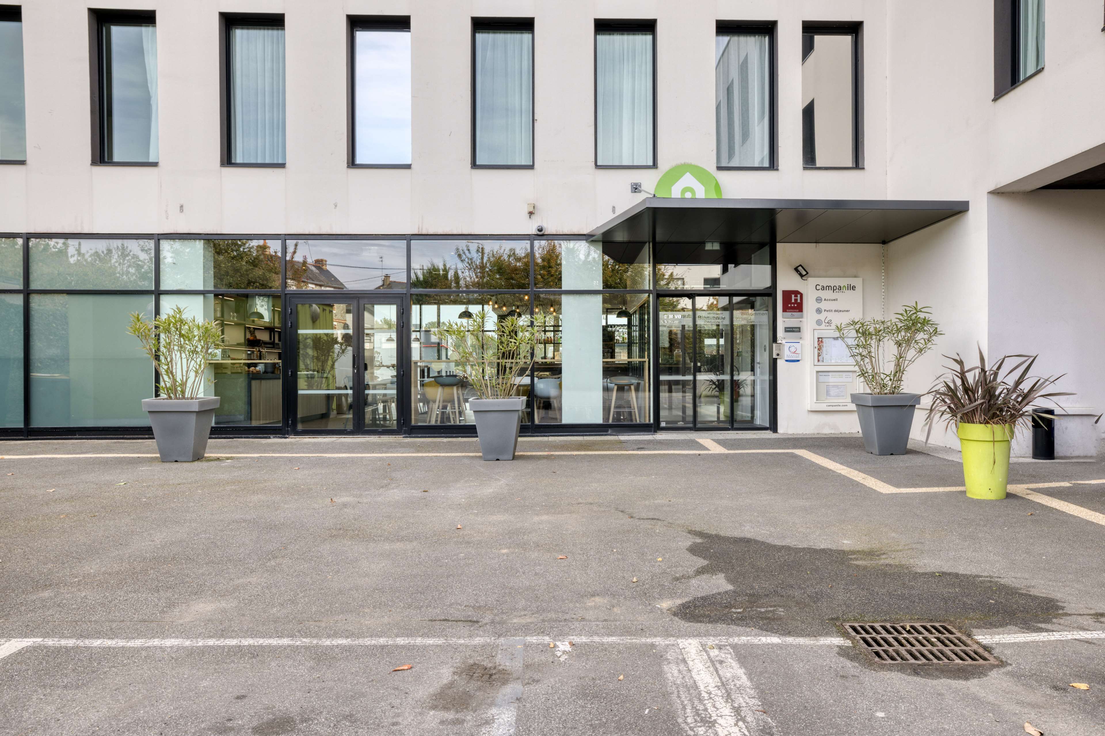 A modern building with a glass entrance, potted plants, and a sign indicating a hotel.