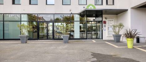 A modern building with a glass entrance, potted plants, and a sign indicating a hotel.