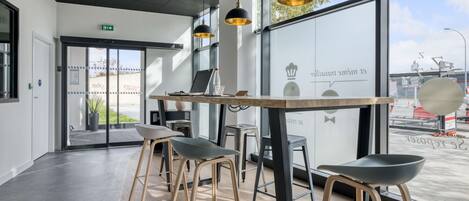 A modern interior with a wooden table, black and gold pendant lights, and metal stools.