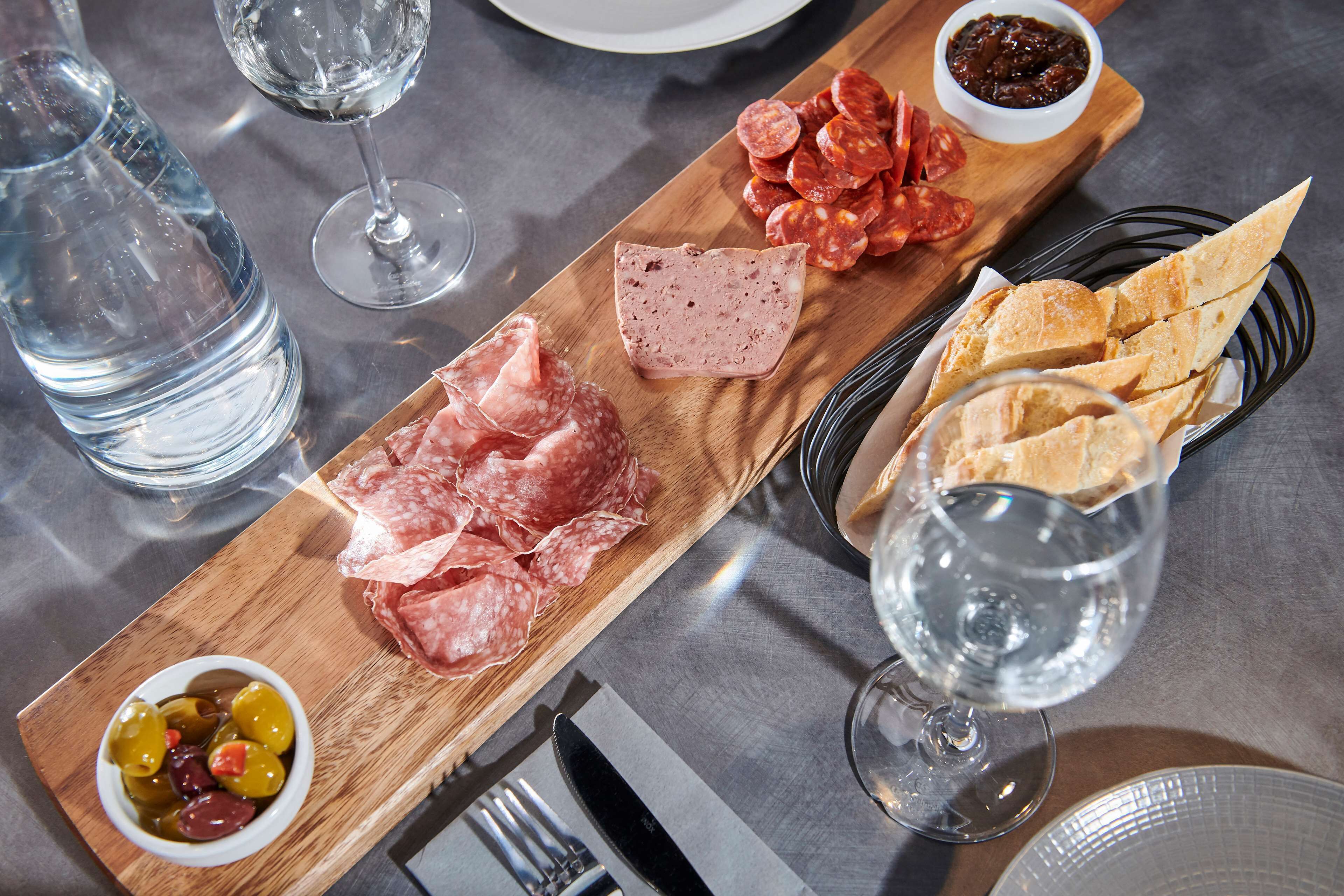 A wooden board with various cured meats, olives, and bread on a table.
