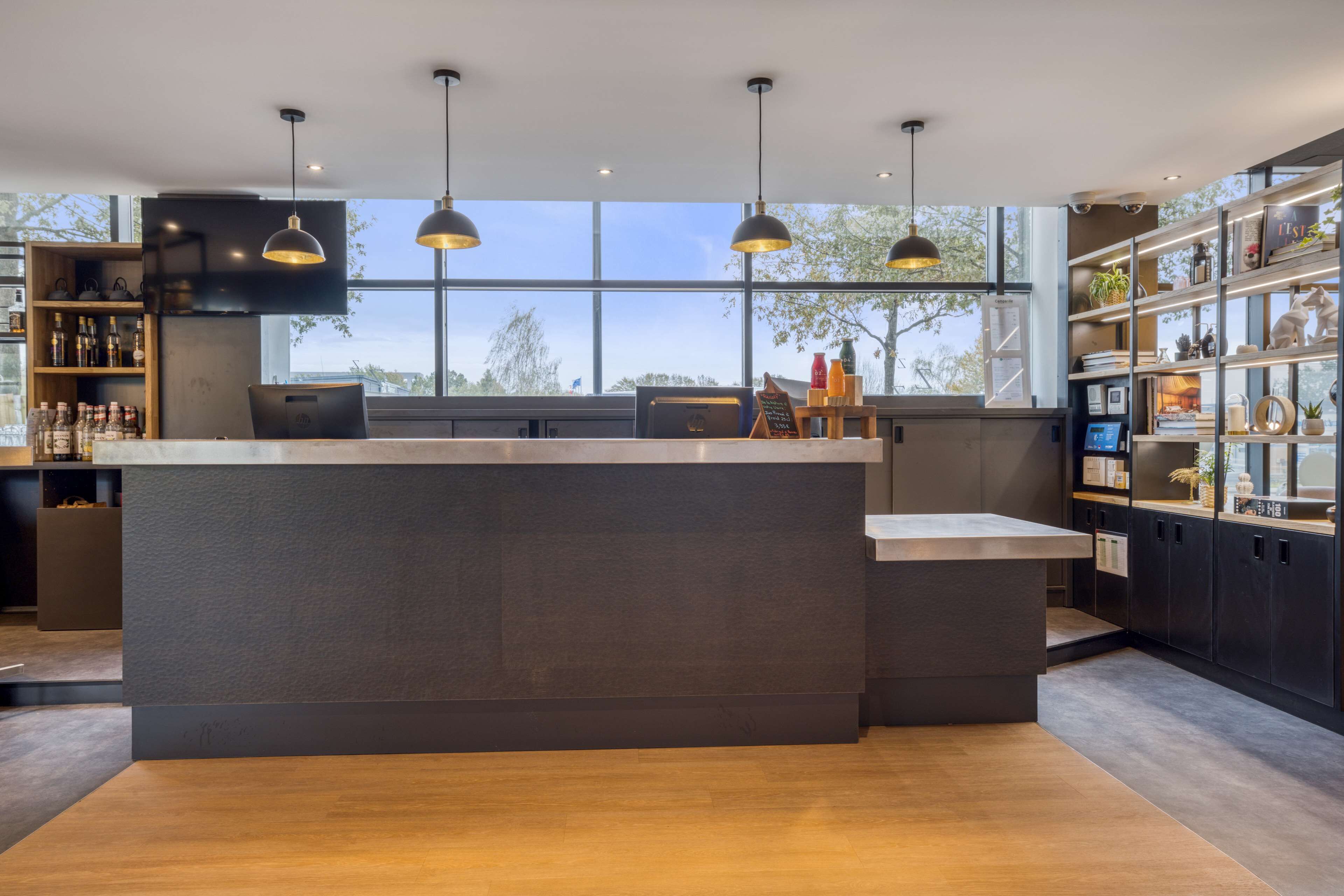 A modern bar area with a large island counter, pendant lighting, and a view of the outdoors through large windows.