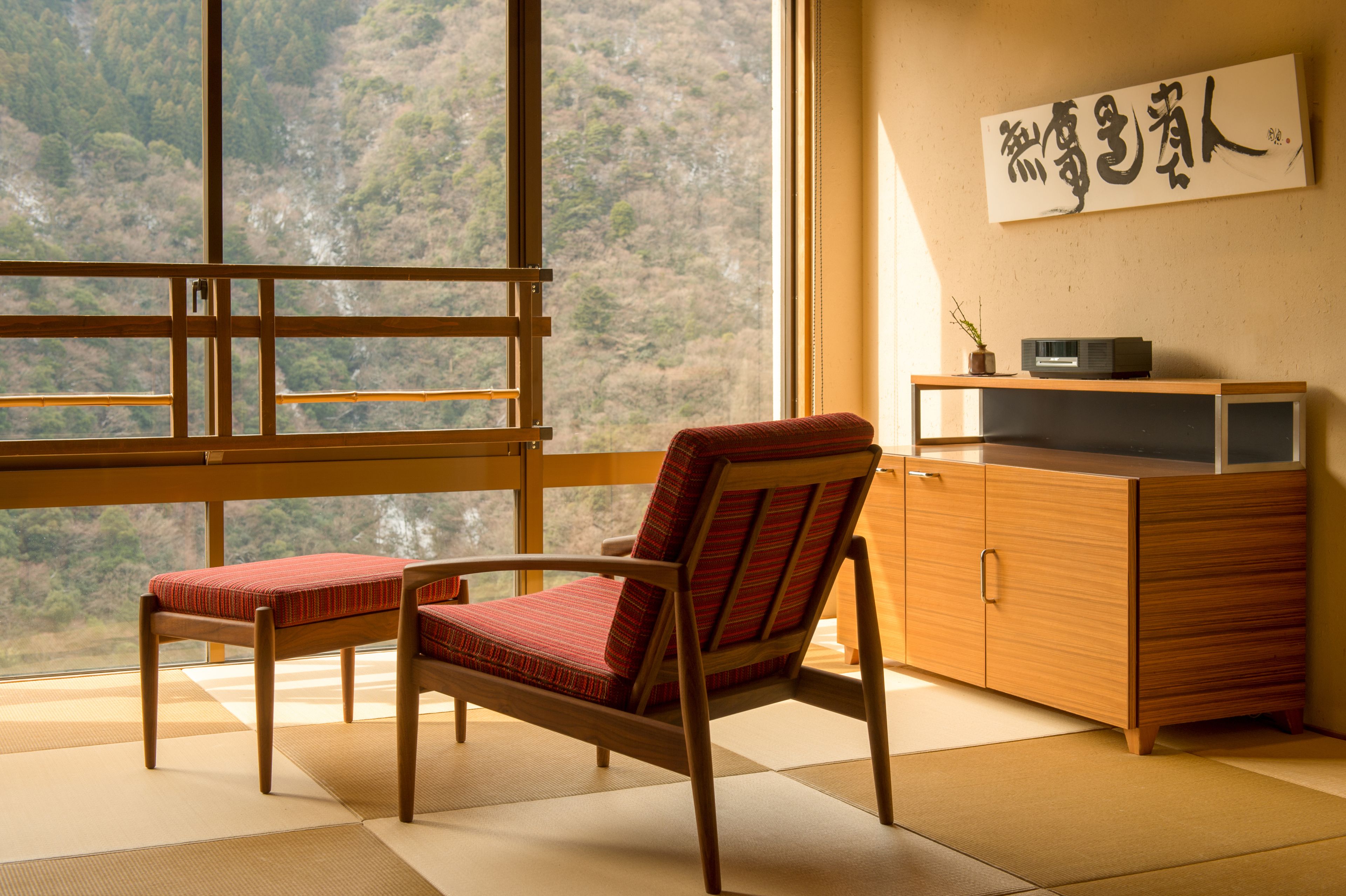 Una habitación japonesa tradicional con suelo de tatami, un escritorio de madera y vistas a una ladera boscosa.