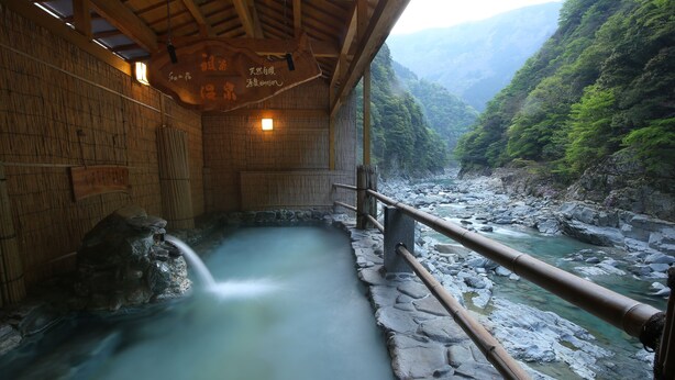 Un baño tradicional de madera con interiores revestidos de piedra y vista a un río.