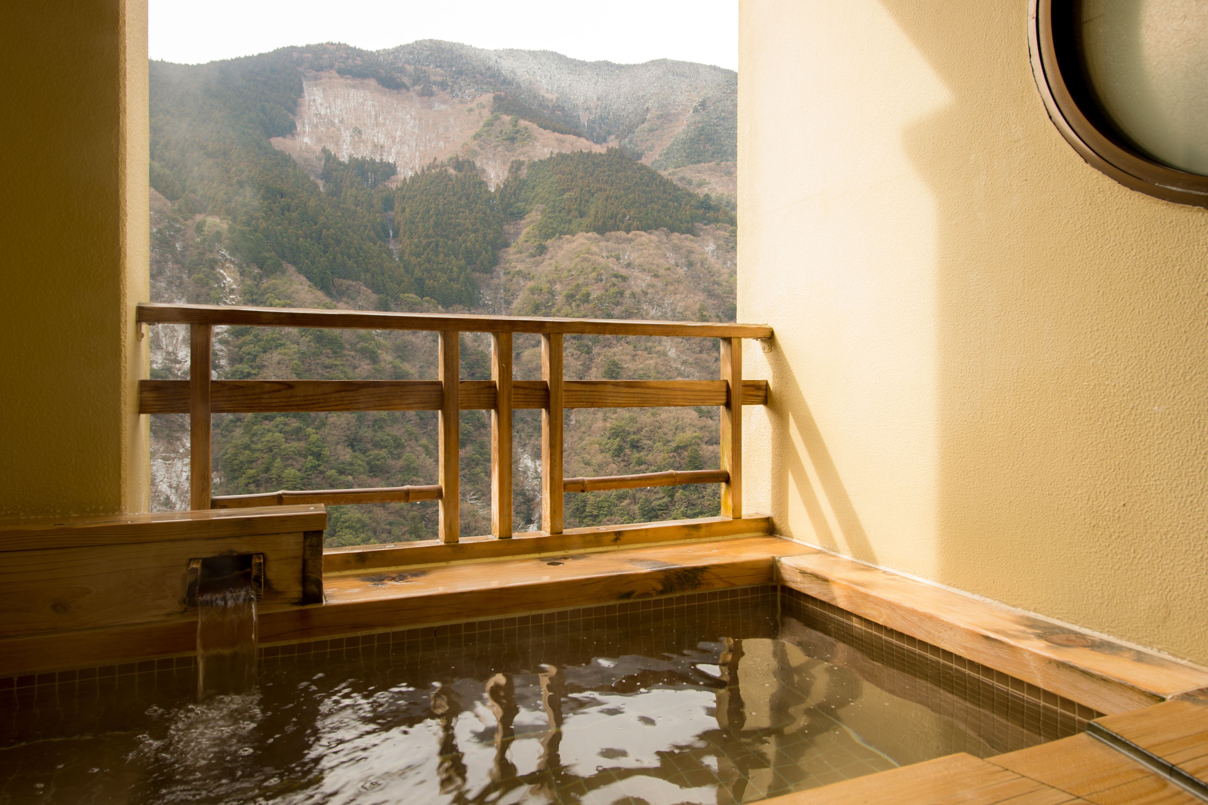 A hot spring bath with a wooden bench and a view of a mountainous landscape.
