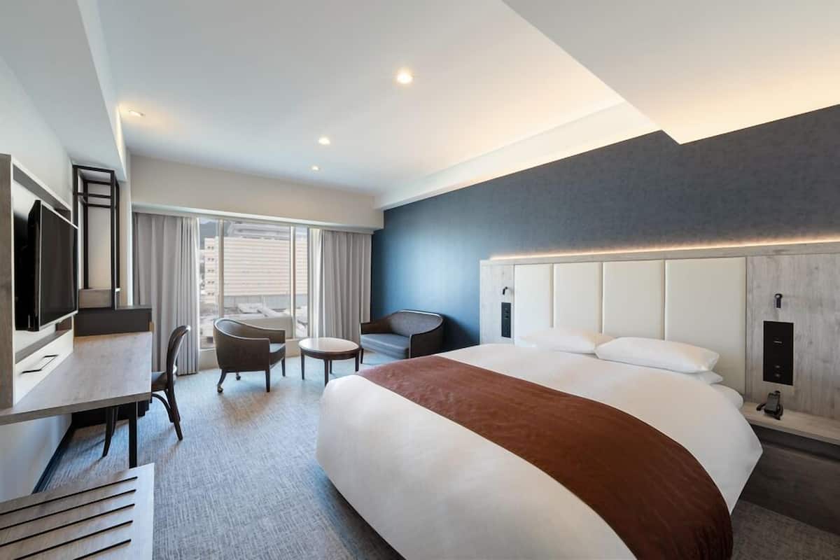 A modern hotel room with a large bed, a desk with a chair, a small round table, and a television.