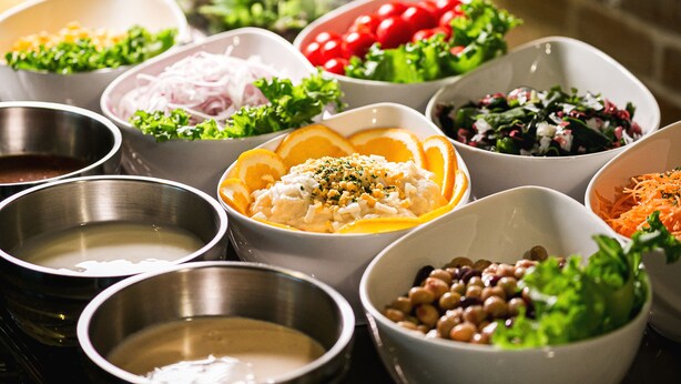 Diversos pratos e alimentos em tigelas, incluindo saladas, feijão e outras opções.