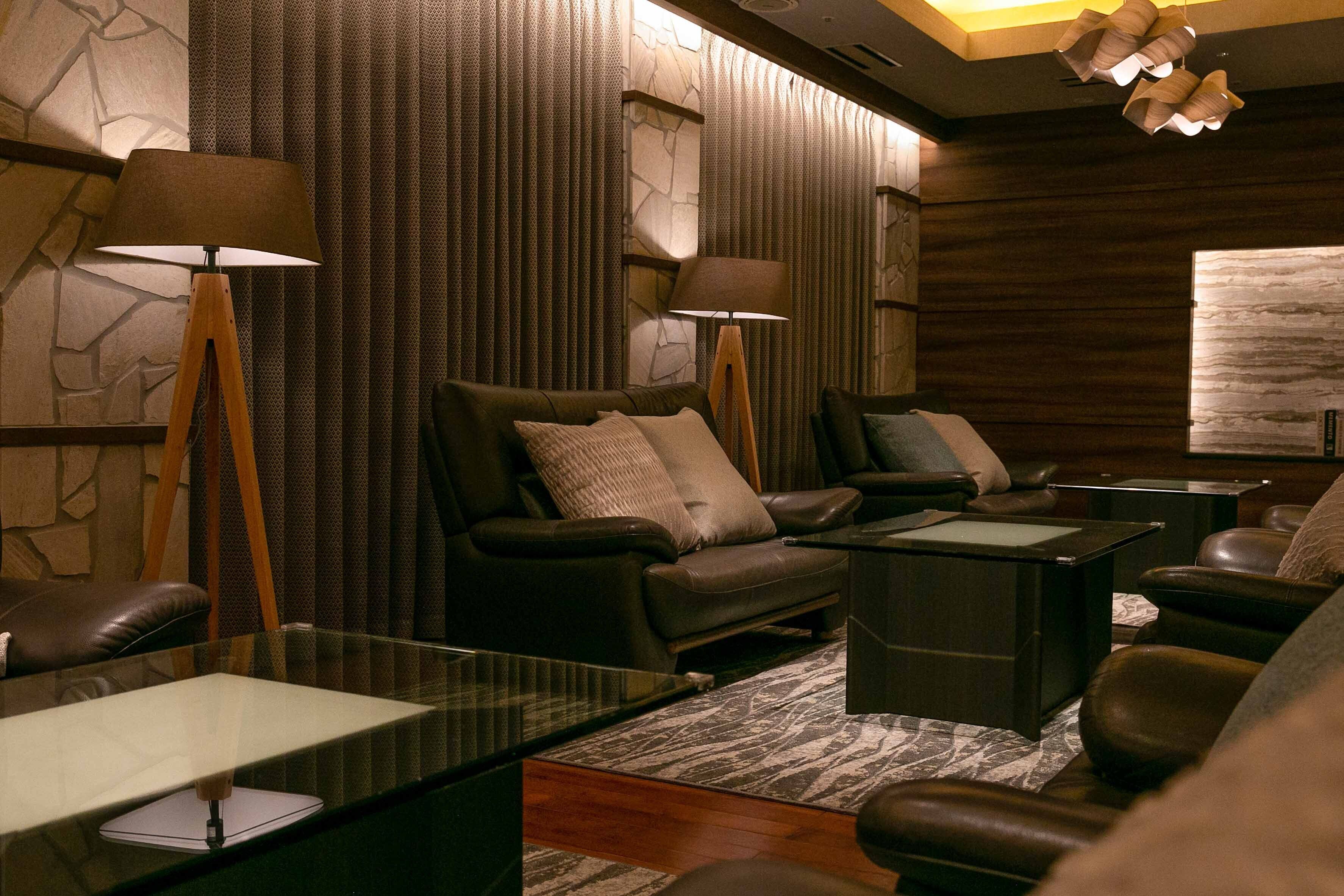 A modern lounge area with leather sofas, a glass coffee table, and two standing lamps.