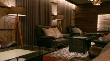 A modern lounge area with leather sofas, a glass coffee table, and two standing lamps.