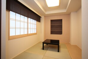 Una habitación con suelo de tatami, una mesa negra, un panel de fusuma y una lámpara en el techo.