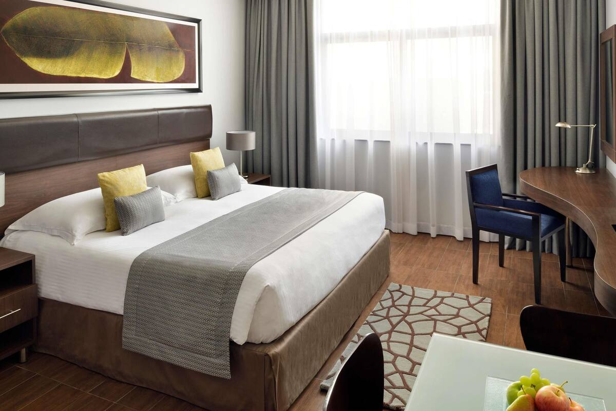 A hotel room with a large bed, a desk, a chair, a lamp, and a painting on the wall.