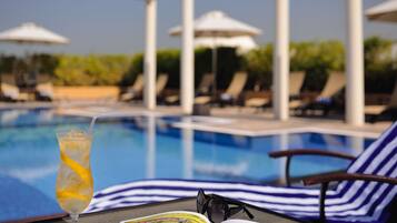 A poolside view with lounge chairs, umbrellas, and a drink on a table.