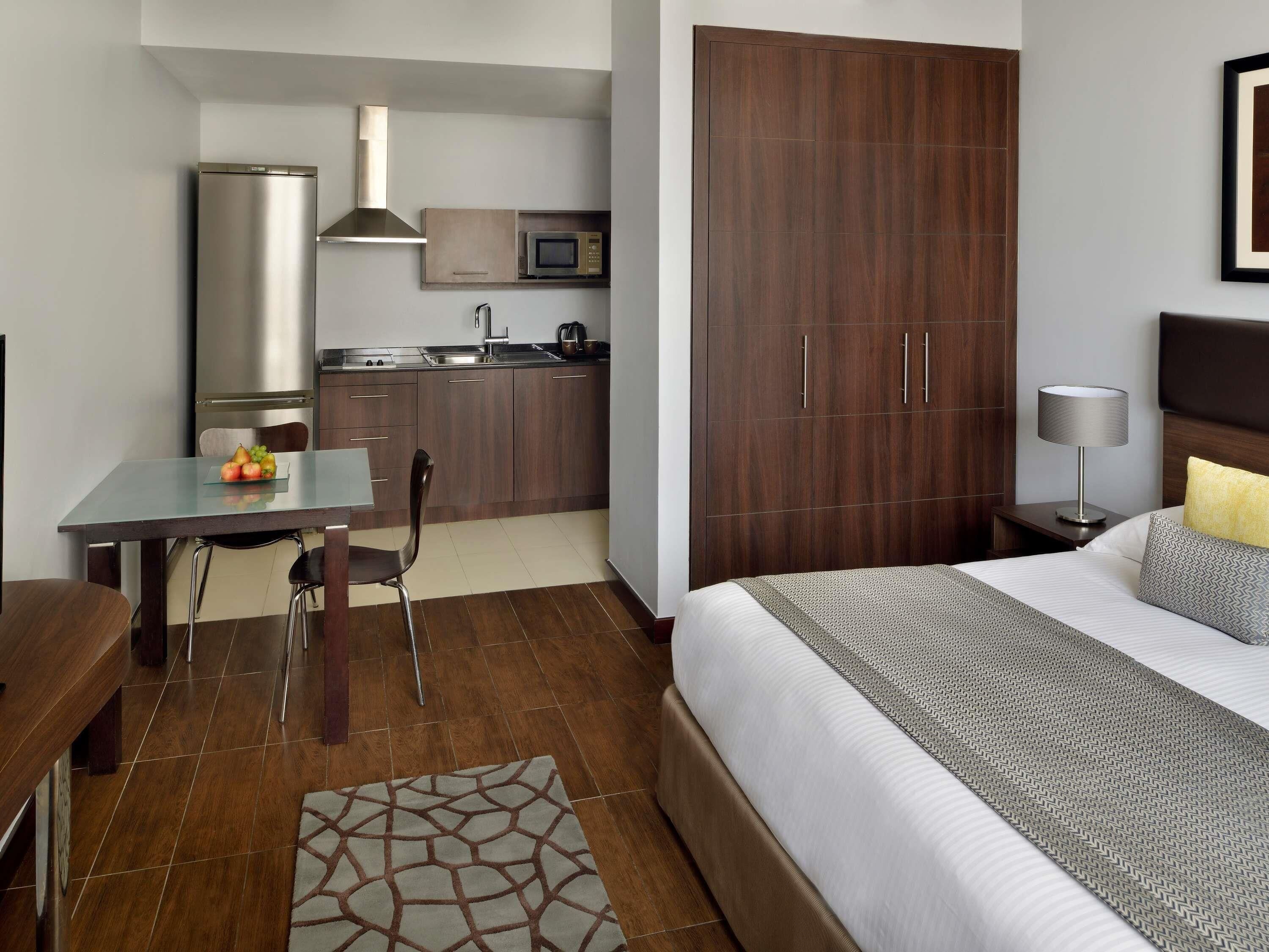Una habitación de hotel compacta con una cama, un escritorio con silla, kitchenette y armario.