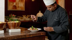 A chef in a uniform preparing food in a kitchen with wooden bowls and a marble countertop. - Movenpick Hotel Apartments Al Mamzar Dubai (Dubai)