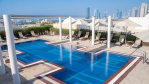 A rooftop pool with lounge chairs and umbrellas, overlooking a cityscape. - Movenpick Hotel Apartments Al Mamzar Dubai (Dubai)