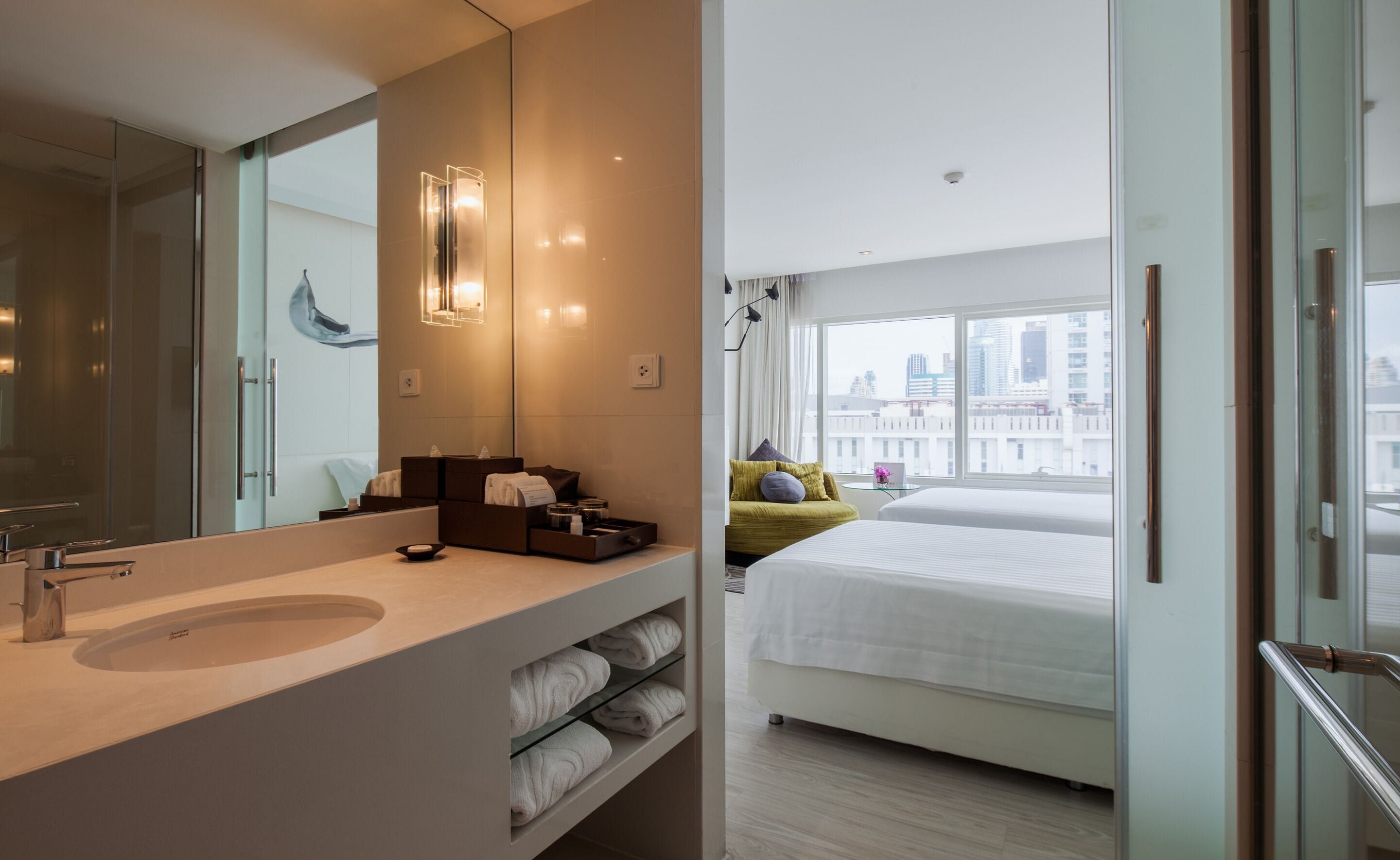 A modern hotel room with a large bathroom vanity, a bed with a city view, and a large mirror.