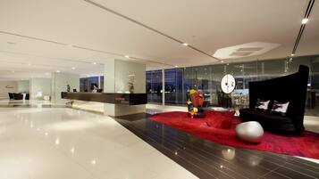 Un hall d’hôtel moderne doté d’un comptoir d’accueil, d’un espace salon et d’un grand mur de verre offrant une vue sur la ville.