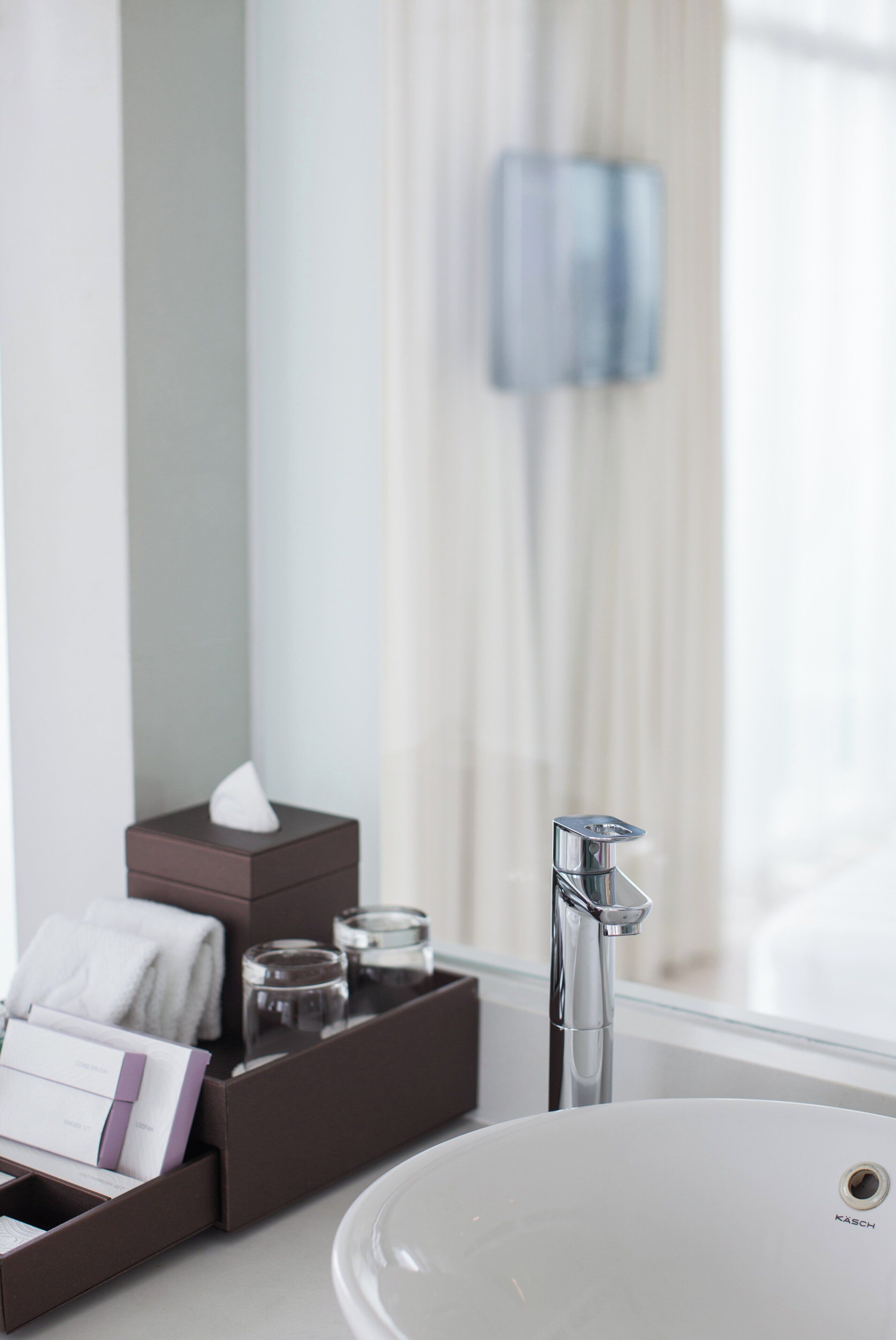 A bathroom with a white sink, a mirror, a towel, and a box of toiletries.