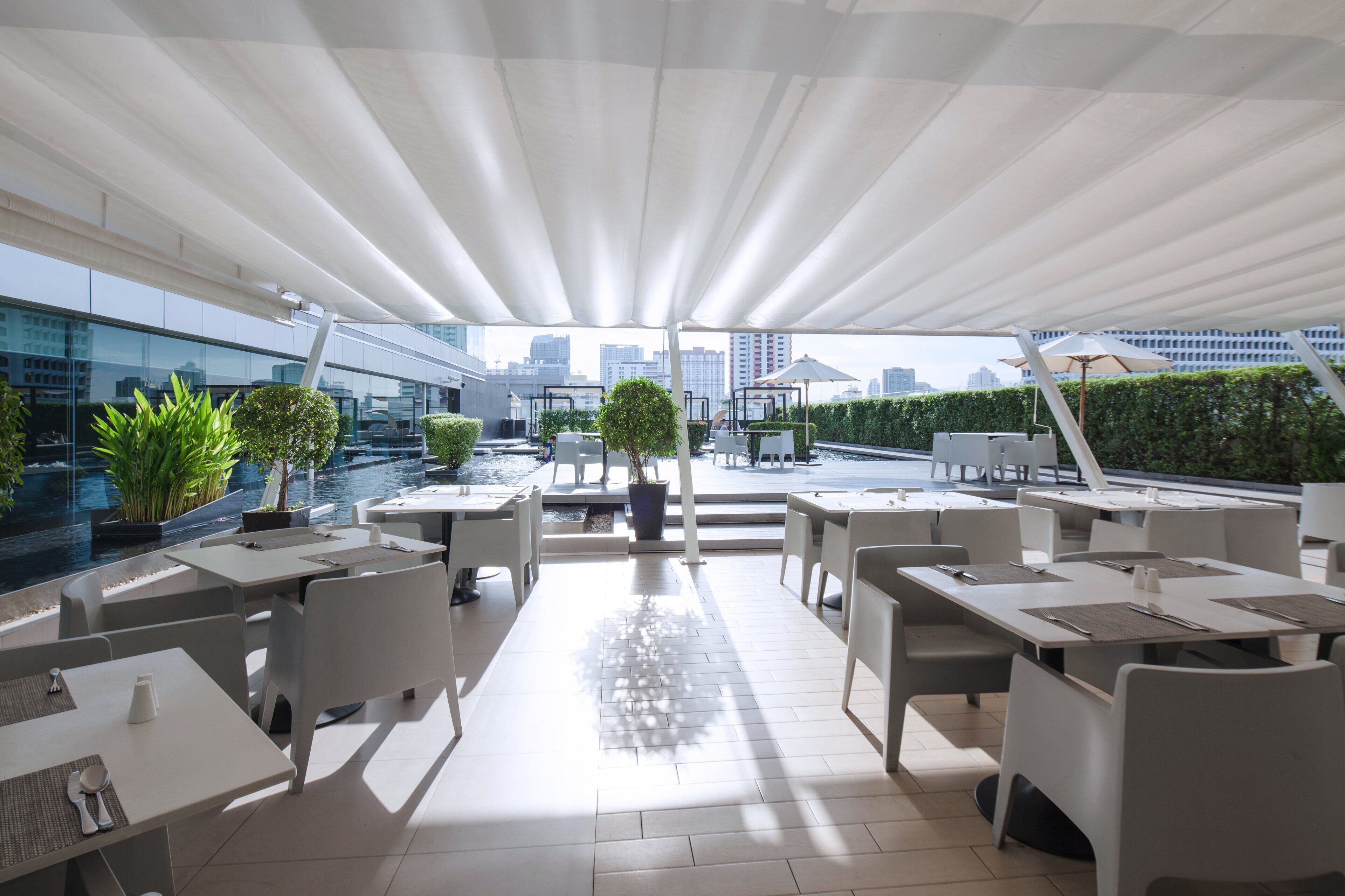 An outdoor dining area with white tables and chairs, potted plants, and a view of the city skyline.