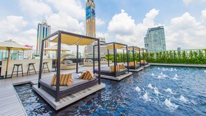 Un espace piscine aménagé sur le toit, avec des chaises longues et des parasols, entouré de grands immeubles.