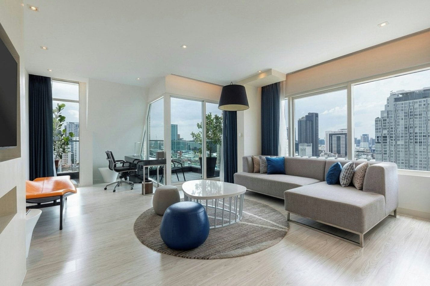 Ein modernes Wohnzimmer mit einer Couch, einem runden Couchtisch und einem Sessel. Es gibt einen Esstisch mit Stühlen und ein großes Fenster mit Blick auf die Stadt.